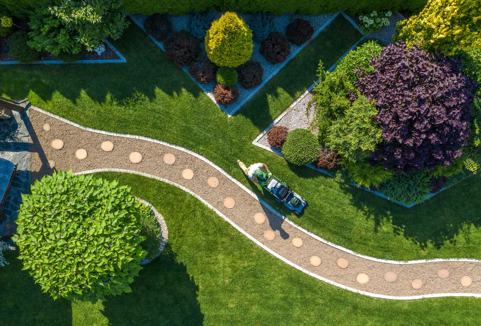 Kaukasischer Gärtner mit Rasenmäher, der den schönen Gartenrasen im Hinterhof trimmt, Luftaufnahme, Garten- und Landschaftsbauindustrie.